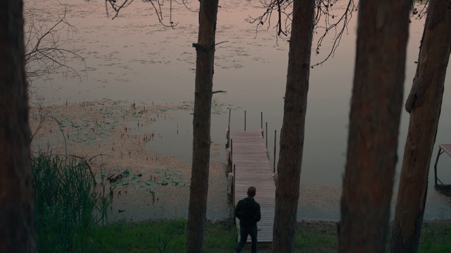 A lone figure among trees beside the water